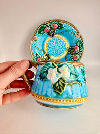 Decorative ceramic cup with floral design held by a hand against a plain background