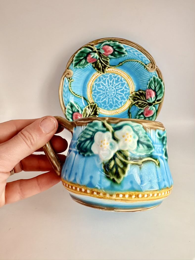 Decorative ceramic cup with floral design held by a hand against a plain background