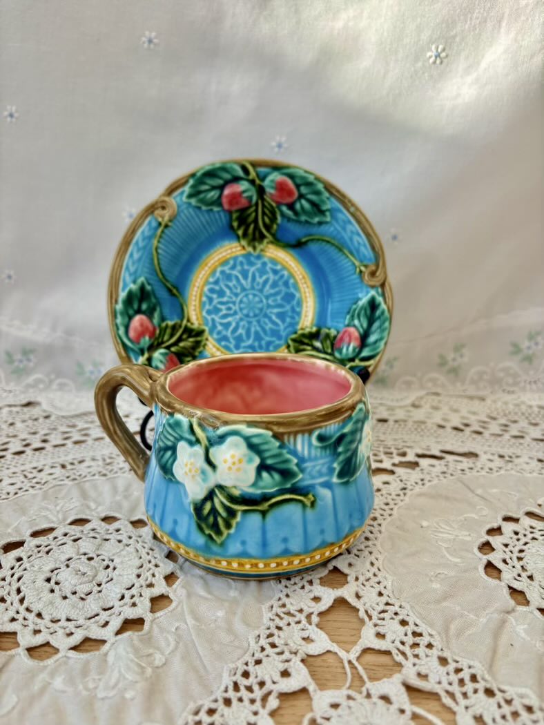 Decorative ceramic cup and saucer with floral design on a lace tablecloth.