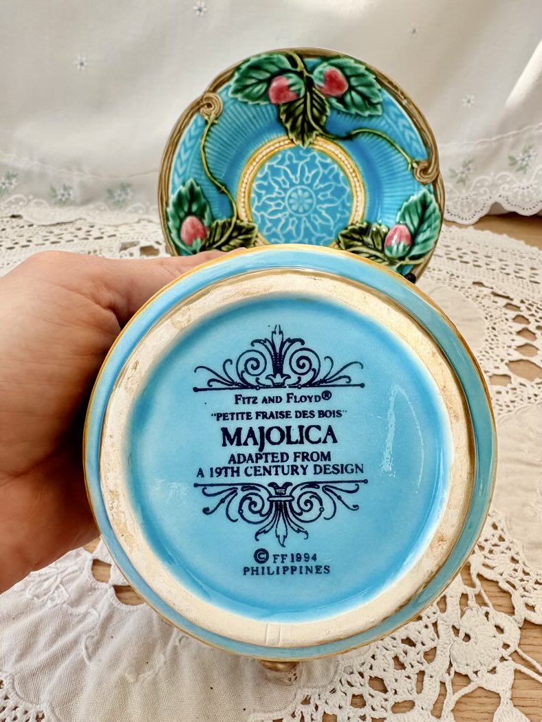 Decorative ceramic dish with blue and gold design, held by a hand on a lace tablecloth.