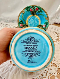Decorative ceramic dish with blue and gold design, held by a hand on a lace tablecloth.