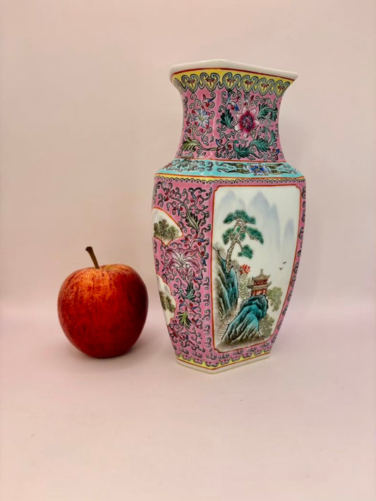 Decorative vase with floral patterns next to an apple on a plain background