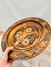 Decorative wooden plate with floral patterns held by a hand on a light background