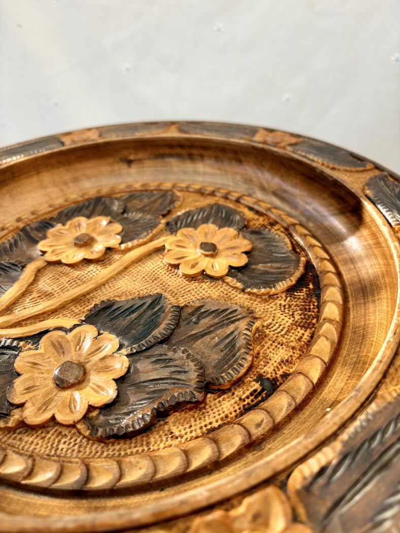 Decorative wooden plate with floral carvings on a plain background