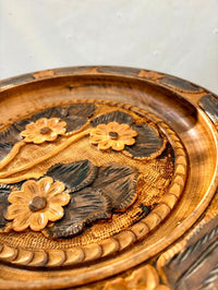 Decorative wooden plate with floral carvings on a plain background