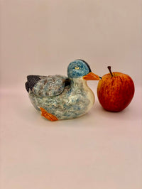 Ceramic duck figurine with a textured surface next to an apple on a plain background