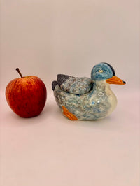 Ceramic duck-shaped container next to an apple on a light pink background