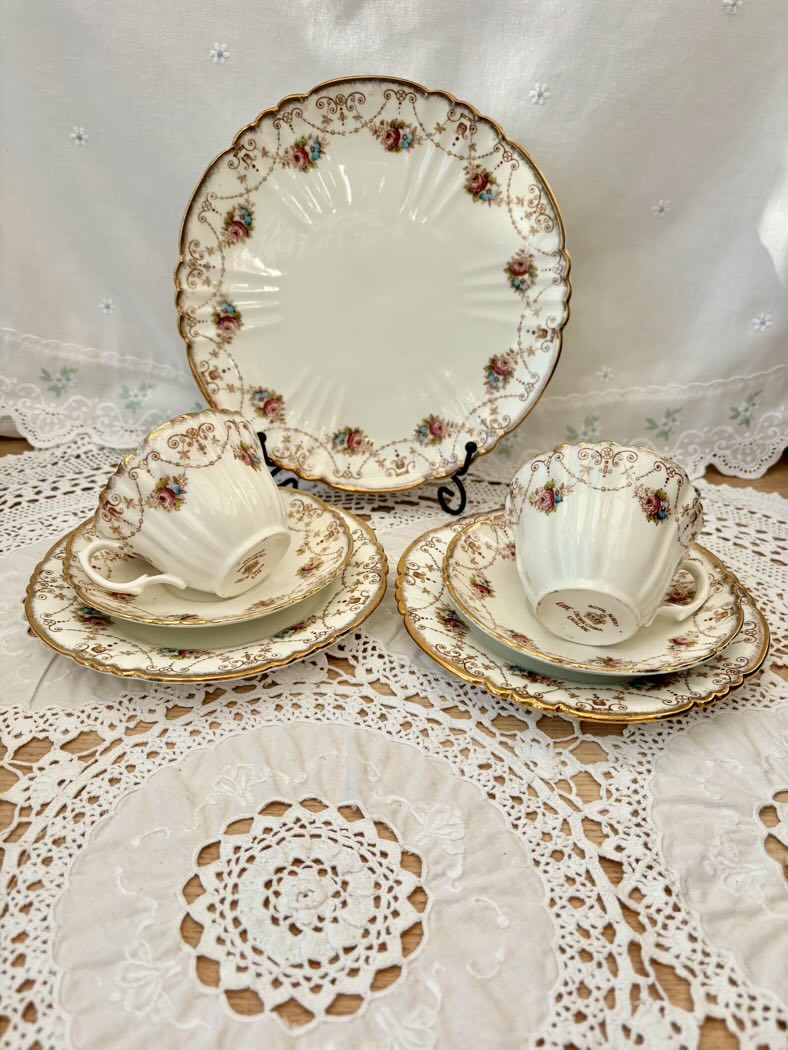 Vintage-style ceramic tea set with floral patterns on a lace tablecloth.