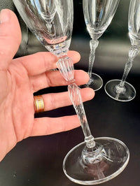 A hand holding one flute by the stem, showing the detailed twisted and ribbed stem with a decorative knop