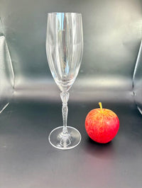 One flute standing upright next to a red apple for size reference