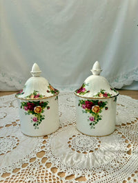 Two floral-decorated ceramic canisters on a lace tablecloth with a white background
