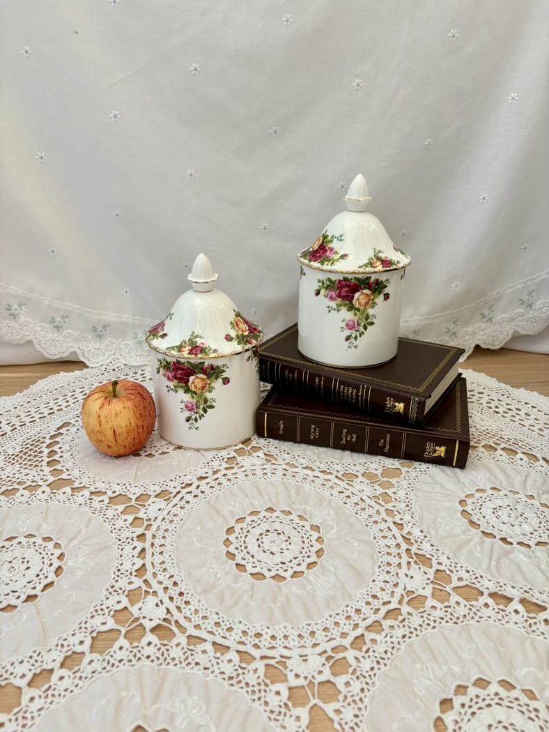 Two ceramic canisters, one on top of the books, and the other one next to a red apple