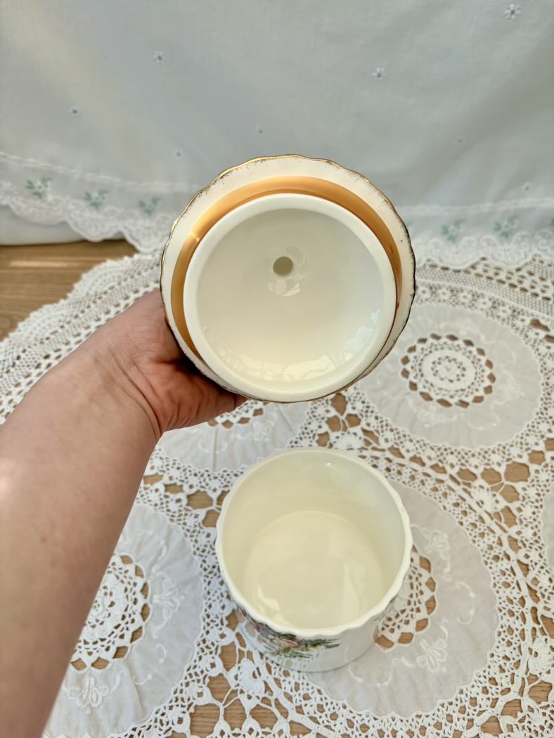 Hand holding a ceramic cup with another cup on a lace tablecloth
