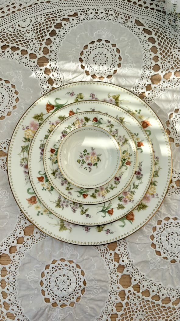 Set of decorative plates with floral patterns on a lace tablecloth.