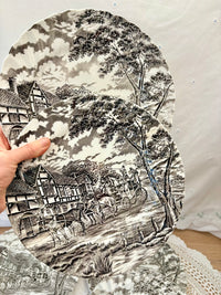 Decorative plate with a black and white landscape design featuring houses and trees.
