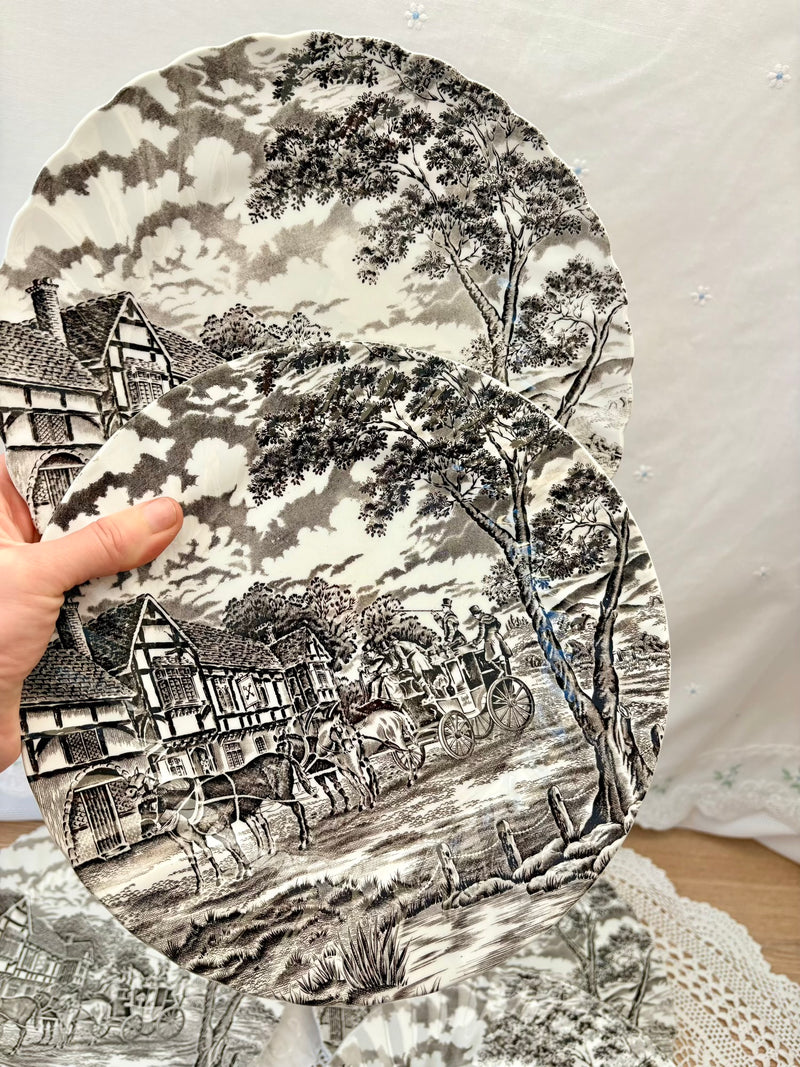 Decorative plate with a black and white landscape design featuring houses and trees.