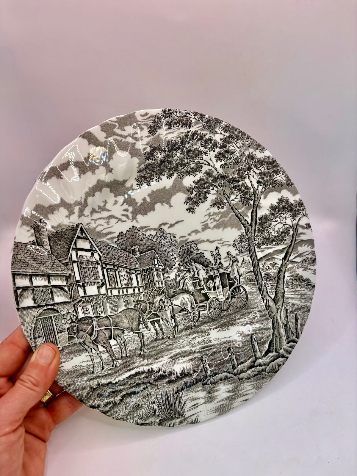Round decorative plate with black and white village scene held by a hand against a light background