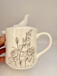 Ceramic teapot with floral designs and a lid held by a hand on a neutral background