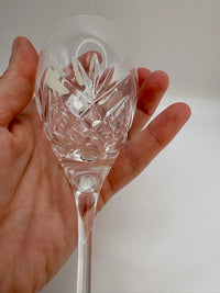Hand holding a clear glass with intricate cut patterns against a plain background