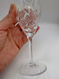 Clear glass wine glass with intricate designs held by a hand on a white background
