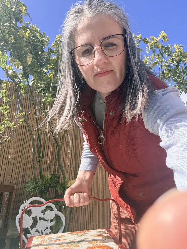 Woman with gray hair and glasses standing outdoors, wearing a red vest.