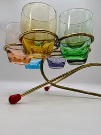 Set of colorful glass tumblers on a brass stand with a white background