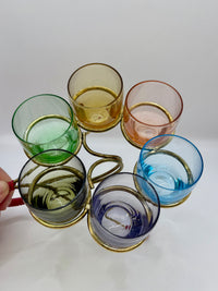 Set of colorful glass tumblers with a gold holder on a white background