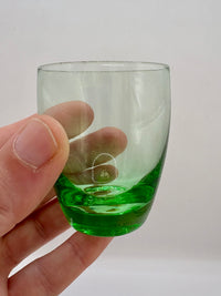 Hand holding a small glass with green liquid against a plain background