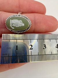 Small oval pendant held between fingers with a ruler for scale
