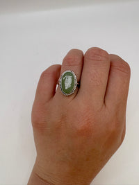 Hand wearing a ring with a green stone and silver band on a white background