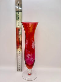 Red glass vase with floral design next to a ruler on a white background