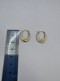 Gold hoop earrings next to a ruler on a gray background