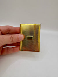 Gold rectangular object held by a hand on a white background