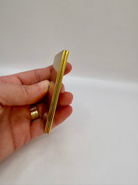 Gold comb held in a hand against a plain background