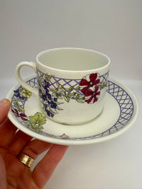 Ceramic cup and saucer with floral design held by a hand against a white background