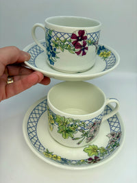 Two floral teacups and saucers held by a hand on a white background