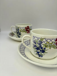 Two ceramic cups with floral patterns on saucers against a white background