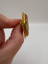 Gold brooch with intricate design held by a hand against a plain background