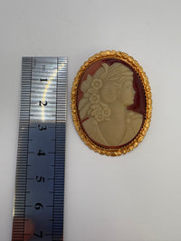 Gold-framed cameo with a ruler for scale on a white background