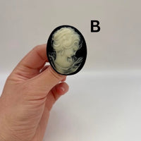 Hand holding a cameo brooch with a white figure on a black background