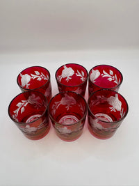 Set of six red glass tumblers with white floral patterns on a white background