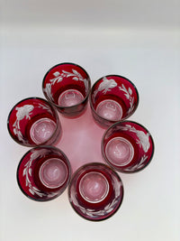 Set of six red glass tumblers with floral etching on a white background