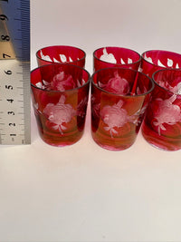 Set of red glass tumblers with floral designs on a white surface, measured against a ruler.