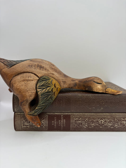 Decorative wooden duckling on top of an ornate book with a plain background