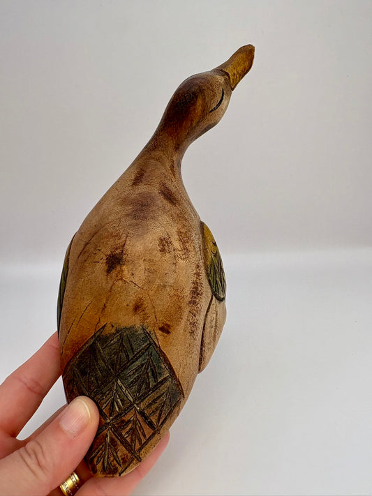 Wooden duck figurine held by a hand against a white background