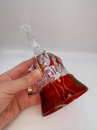 Hand holding a decorative glass bell with intricate designs on a plain background