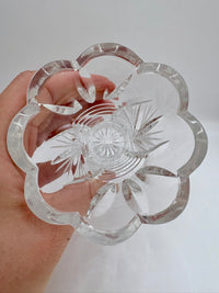 Clear crystal dish with floral design held by a hand against a white background