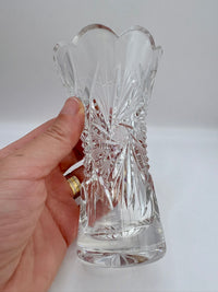 Hand holding a clear cut glass vase against a white background