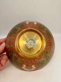 Decorative bowl with gold interior and intricate patterns, held by a hand on a white background.