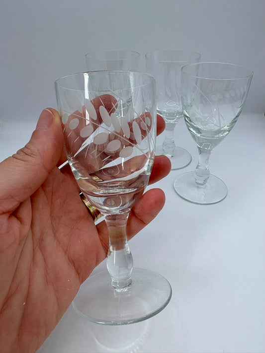 Hand holding a clear glass with etched design against a white background